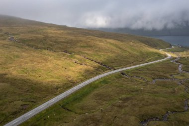 Yazın sonunda Faroe Adaları 'nın yemyeşil yeşil manzaraları arasında dolambaçlı bir yolun çarpıcı görüntüsü..