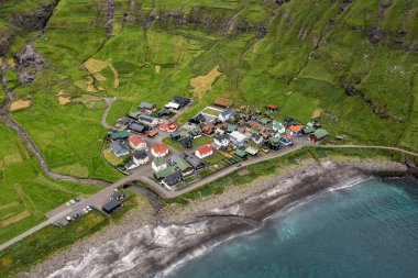 Faroe Adaları 'ndaki büyüleyici bir sahil köyünün yemyeşil manzaraları ve dramatik uçurumlarla çevrili nefes kesici görüntüsü..