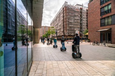 Segways 'deki bir grup turist Hamburgs sokaklarında geziniyor, modern binalar ve yaz atmosferini sergiliyorlar..