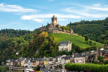 Cochem Kalesi 'nin göz kamaştırıcı yaz manzarası Moselle Nehri' nin üzerine tünemiş, yemyeşil üzüm bağları ve büyüleyici köy sokaklarıyla çevrili..