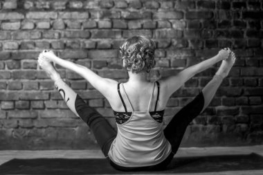 Siyah taytlı ve huş ağacından tişörtlü genç bir kız bir Asana 'da tuğla bir duvarın arkasında oturuyor. Yüksek kalite fotoğraf