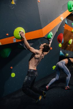 Güzel şişirilmiş vücudu olan genç, atletik bir adam tırmanma salonundaki kayaya tırmanıyor. Yüzünde duygular var. Yüksek kalite fotoğraf