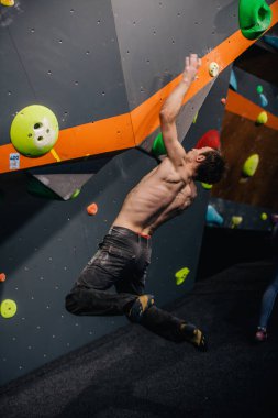 Güzel şişirilmiş vücudu olan genç, atletik bir adam tırmanma salonundaki kayaya tırmanıyor. Yüzünde duygular var. Yüksek kalite fotoğraf