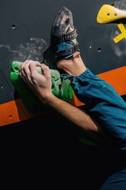 Güzel şişirilmiş vücudu olan genç, atletik bir adam tırmanma salonundaki kayaya tırmanıyor. Yüzünde duygular var. Yüksek kalite fotoğraf