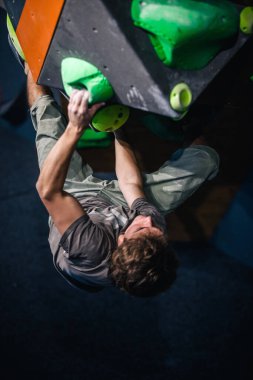 Güzel şişirilmiş vücudu olan genç, atletik bir adam tırmanma salonundaki kayaya tırmanıyor. Yüzünde duygular var. Yüksek kalite fotoğraf