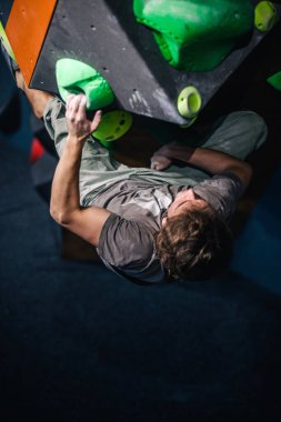 Güzel şişirilmiş vücudu olan genç, atletik bir adam tırmanma salonundaki kayaya tırmanıyor. Yüzünde duygular var. Yüksek kalite fotoğraf