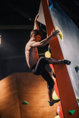 Güzel şişirilmiş vücudu olan genç, atletik bir adam tırmanma salonundaki kayaya tırmanıyor. Yüzünde duygular var. Yüksek kalite fotoğraf