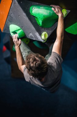 Güzel şişirilmiş vücudu olan genç, atletik bir adam tırmanma salonundaki kayaya tırmanıyor. Yüzünde duygular var. Yüksek kalite fotoğraf