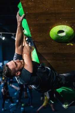 Güzel şişirilmiş vücudu olan genç, atletik bir adam tırmanma salonundaki kayaya tırmanıyor. Yüzünde duygular var. Yüksek kalite fotoğraf