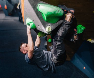 Güzel şişirilmiş vücudu olan genç, atletik bir adam tırmanma salonundaki kayaya tırmanıyor. Yüzünde duygular var. Yüksek kalite fotoğraf