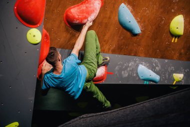 Güzel şişirilmiş vücudu olan genç, atletik bir adam tırmanma salonundaki kayaya tırmanıyor. Yüzünde duygular var. Yüksek kalite fotoğraf