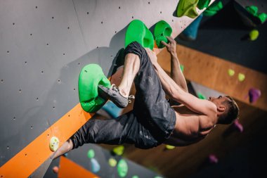 Güzel şişirilmiş vücudu olan genç, atletik bir adam tırmanma salonundaki kayaya tırmanıyor. Yüzünde duygular var. Yüksek kalite fotoğraf