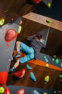 Gri tişörtlü ve mavi şortlu genç, güçlü bir adam bir tırmanış merkezinde kayaya tırmanıyor. Yüksek kalite fotoğraf
