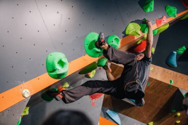 Güzel şişirilmiş vücudu olan genç, atletik bir adam tırmanma salonundaki kayaya tırmanıyor. Yüzünde duygular var. Yüksek kalite fotoğraf