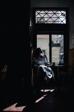 Beyaz elbiseli genç kız güneşin altında pencerenin yanındaki bir kafede kahve içiyor. Siluet. Yüksek kalite fotoğraf