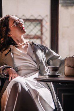 Beyaz elbiseli genç kız güneşin altında pencerenin yanındaki bir kafede kahve içiyor. Siluet. Yüksek kalite fotoğraf