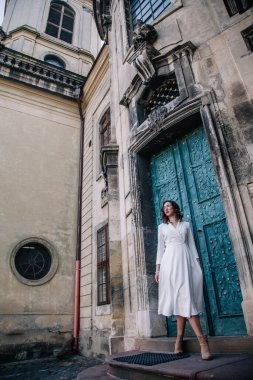 Beyaz elbiseli, gri pelerinli genç, güzel bir kız tapınağın eski gri kapılarının yanında poz veriyor. Yüksek kalite fotoğraf