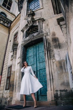 Beyaz elbiseli, gri pelerinli genç, güzel bir kız tapınağın eski gri kapılarının yanında poz veriyor. Yüksek kalite fotoğraf