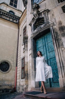 Beyaz elbiseli, gri pelerinli genç, güzel bir kız tapınağın eski gri kapılarının yanında poz veriyor. Yüksek kalite fotoğraf