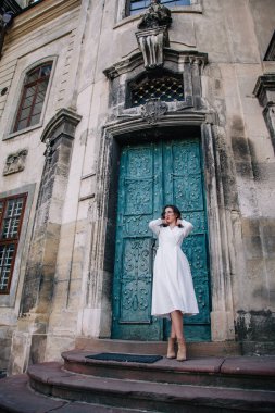Beyaz elbiseli, gri pelerinli genç, güzel bir kız tapınağın eski gri kapılarının yanında poz veriyor. Yüksek kalite fotoğraf