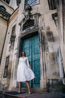 Beyaz elbiseli, gri pelerinli genç, güzel bir kız tapınağın eski gri kapılarının yanında poz veriyor. Yüksek kalite fotoğraf