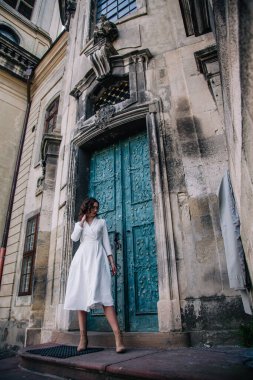 Beyaz elbiseli, gri pelerinli genç, güzel bir kız tapınağın eski gri kapılarının yanında poz veriyor. Yüksek kalite fotoğraf