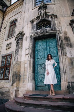 Beyaz elbiseli, gri pelerinli genç, güzel bir kız tapınağın eski gri kapılarının yanında poz veriyor. Yüksek kalite fotoğraf