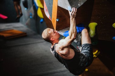 Siyah atletik tişörtlü genç adam tırmanma yarışmasında duvara tırmanıyor. Yüksek kalite fotoğraf