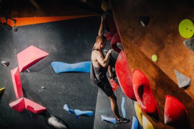 Siyah atletik tişörtlü genç adam tırmanma yarışmasında duvara tırmanıyor. Yüksek kalite fotoğraf
