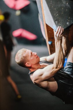 Siyah atletik tişörtlü genç adam tırmanma yarışmasında duvara tırmanıyor. Yüksek kalite fotoğraf