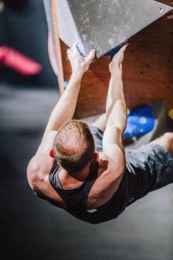 Siyah atletik tişörtlü genç adam tırmanma yarışmasında duvara tırmanıyor. Yüksek kalite fotoğraf