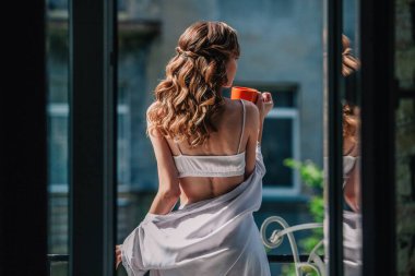 Düğünden önce beyaz dantelli iç çamaşırlarıyla genç, sıska bir gelin otel odasının balkonunda turuncu bir fincandan kahve içiyor. Yüksek kalite fotoğraf