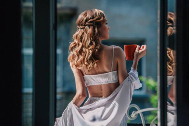 Düğünden önce beyaz dantelli iç çamaşırlarıyla genç, sıska bir gelin otel odasının balkonunda turuncu bir fincandan kahve içiyor. Yüksek kalite fotoğraf