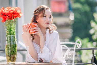 Düğünden önce beyaz dantelli iç çamaşırlarıyla genç, narin bir gelin bir otel odasının balkonunda otururken portakallı fincandan kahve içiyor. Yüksek kalite fotoğraf