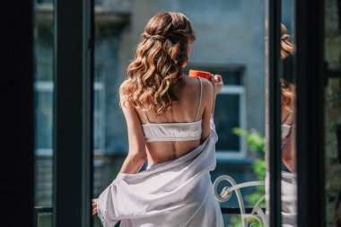 Düğünden önce beyaz dantelli iç çamaşırlarıyla genç, sıska bir gelin otel odasının balkonunda turuncu bir fincandan kahve içiyor. Yüksek kalite fotoğraf