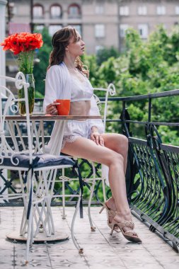 Düğünden önce beyaz dantelli iç çamaşırlarıyla genç, narin bir gelin bir otel odasının balkonunda otururken portakallı fincandan kahve içiyor. Yüksek kalite fotoğraf