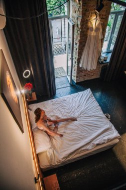 Genç, güzel bir gelin, sabahleyin otel odasında uzanmadan önce beyaz dantelli iç çamaşırlarıyla. Yüksek kalite fotoğraf