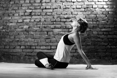 Turkuaz tişörtlü, siyah taytlı, ince atletik bir kız tuğla duvarın arkasında yoga yapıyor. Yüksek kalite fotoğraf