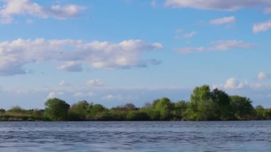 The river flows in a fast stream with the blue sky with clouds, and green trees on the opposite bank in the background