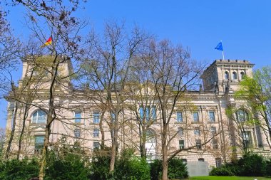 Berlin 'deki Reichstag' ın yanına park et. Ağaçların arkasında Bundestag 'ın kubbeleri Almanya ve Avrupa Birliği' nin bayrakları var..