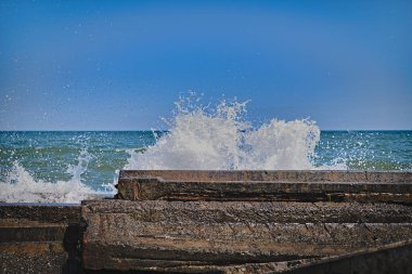 Arkaplanda gökyüzünün mavi renginde granit sette kırılan dalgalardan sıçrama