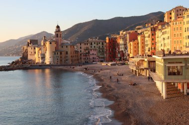 Camogli, Italy - January 27, 2023: Beautiful old mediterranean town at the sunrise time with illumination during winter days.People enjoying the evening at the beach with beautiful sunset background