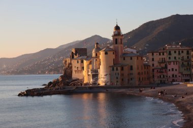 Camogli, Italy - January 27, 2023: Beautiful old mediterranean town at the sunrise time with illumination during winter days.People enjoying the evening at the beach with beautiful sunset background