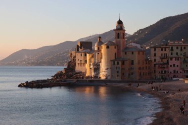 Camogli, Italy - January 27, 2023: Beautiful old mediterranean town at the sunrise time with illumination during winter days.People enjoying the evening at the beach with beautiful sunset background