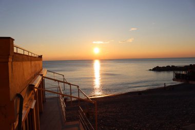 Camogli, Italy - January 27, 2023: Beautiful old mediterranean town at the sunrise time with illumination during winter days.People enjoying the evening at the beach with beautiful sunset background