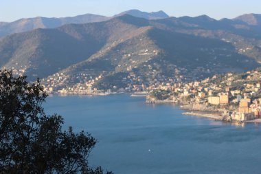 Camogli, Italy - January 27, 2023: Beautiful old mediterranean town at the sunrise time with illumination during winter days. People enjoying the evening at the beach with beautiful sunset background