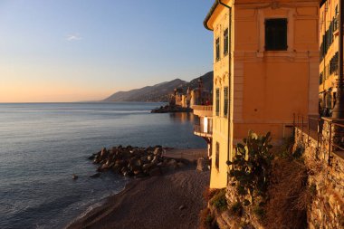 Camogli, Italy - January 27, 2023: Beautiful old mediterranean town at the sunrise time with illumination during winter days. People enjoying the evening at the beach with beautiful sunset background