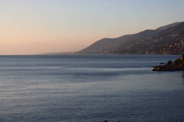 Camogli, Italy - January 27, 2023: Beautiful old mediterranean town at the sunrise time with illumination during winter days. People enjoying the evening at the beach with beautiful sunset background