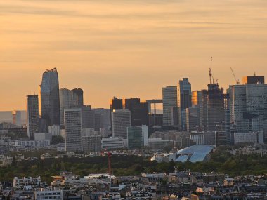 Paris, Fransa - 12 Nisan 2024: Modern gökdelenler ve eski binalar arasındaki altın saat boyunca Paris şehrine havadan bakış. Şehrin üzerinde güzel bir gün batımı yansıyor binalara.