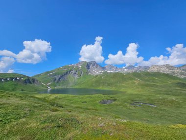 La Thuile, Val D 'Aosta, Temmuz 02 2025: Alplere panoramik manzara, küçük doğal bir göle yansıyan güzel yeşil manzara. Bulutlu güzel mavi gökyüzü. Biraz karlı dağlar. La Thuile köyünün havadan görünüşü.